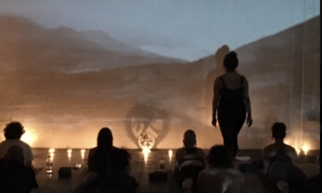 Candlelit yoga class with instructor leading relaxation in dark studio, peaceful meditation ambiance and warm lighting