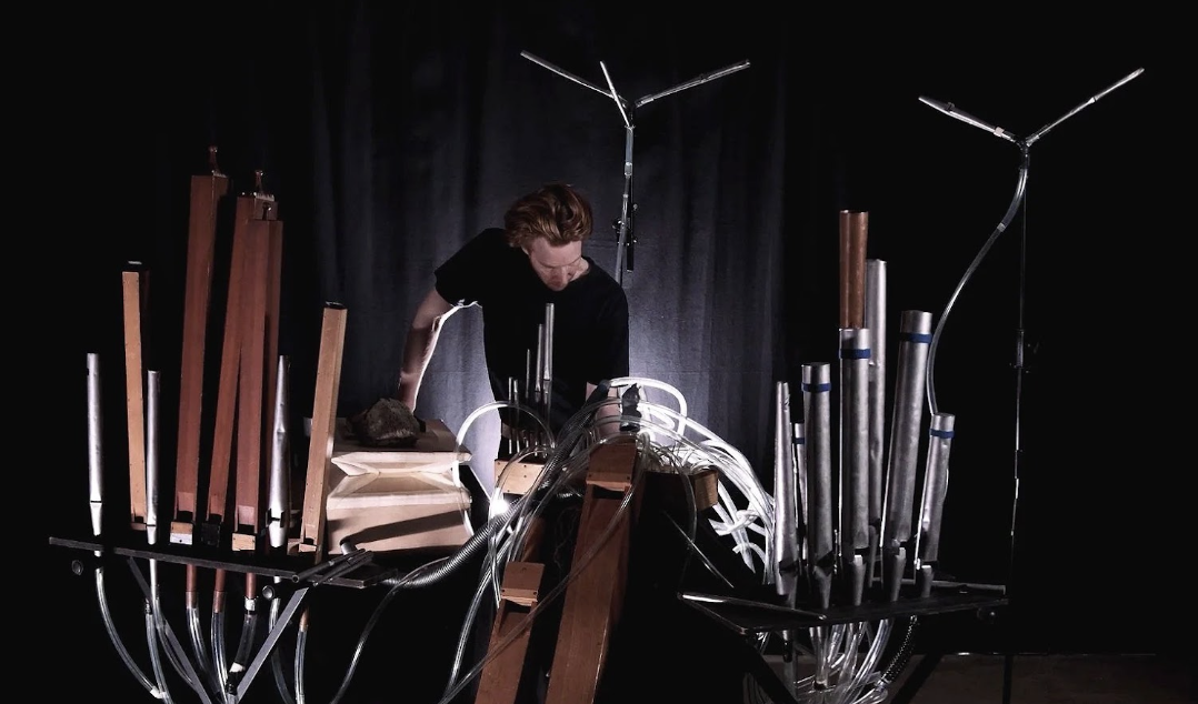 Musician performing on experimental pipe organ sound art installation with tubes on dark stage